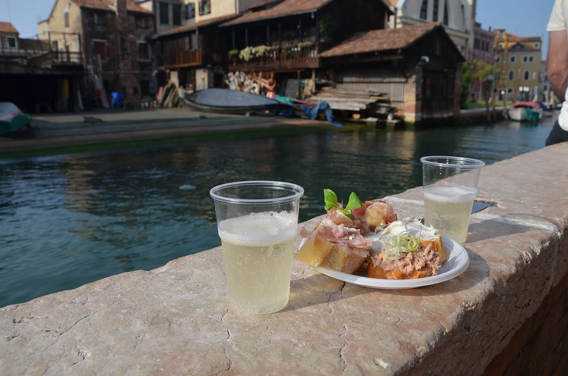 Cicchetti e un bicchiere di vino su un parapetto affacciato su un canale