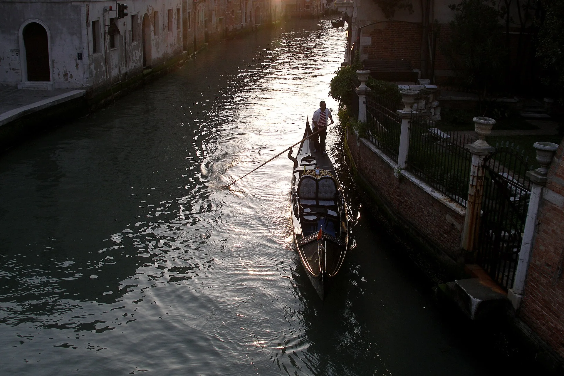 Una gondola risale un rio stretto di Venezia nella luce della sera
